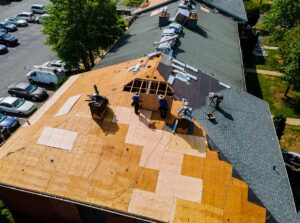 Person carefully stepping across a dry shingle roof beside a secured extension ladder.