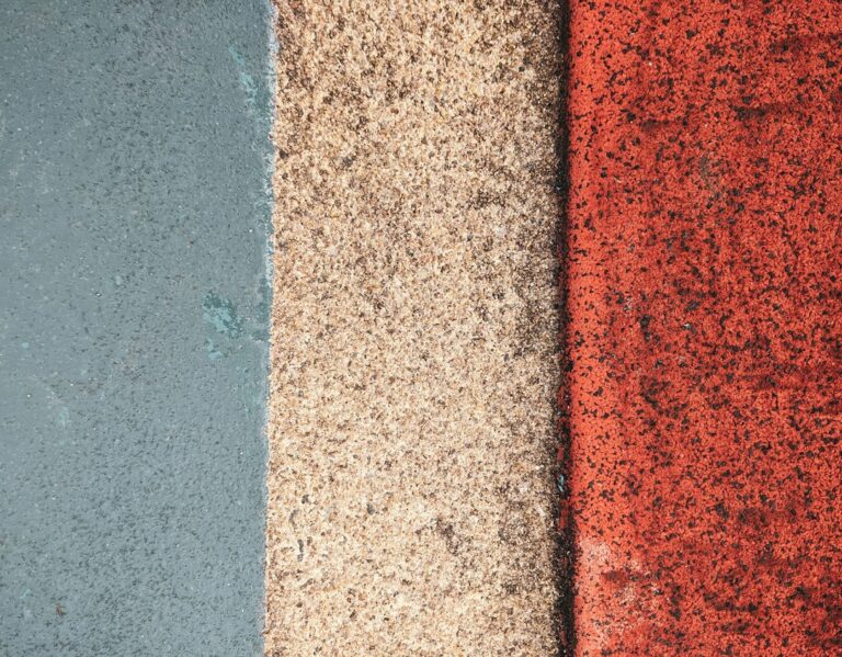 Person comparing a new asphalt shingle sample with weathered shingles beside a residential roof.